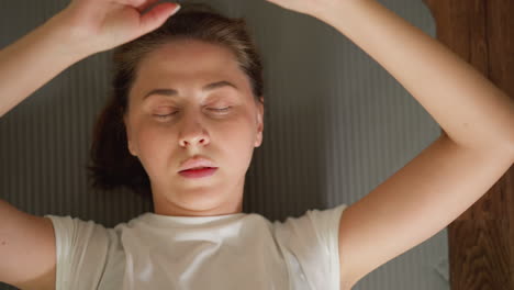 fatigued female reclines on mat post-training. drained woman exhales while resting on floor in home gym. attractive athlete taking break from exercising