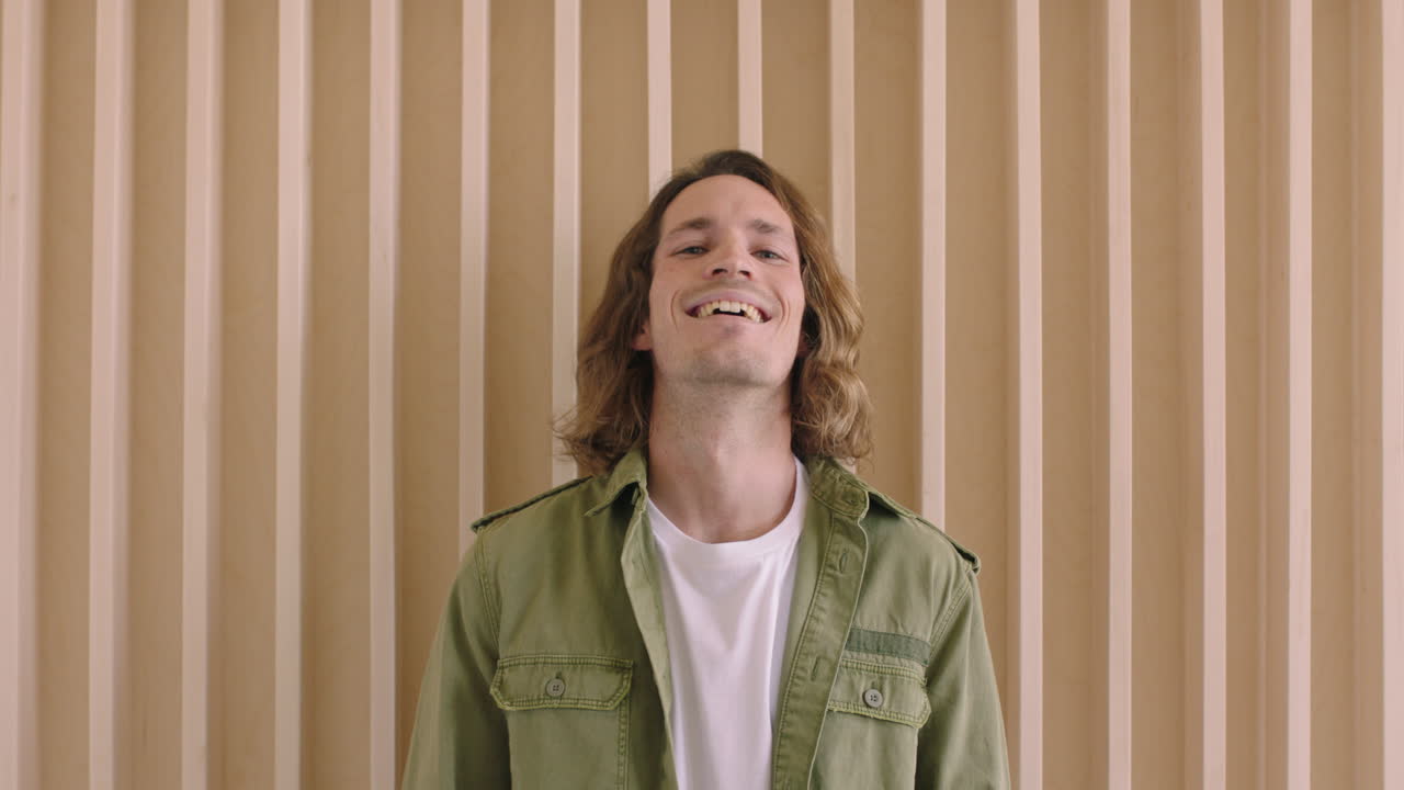 예쁜 젊은 백인 남자의 초상화 웃고 즐겁고 자신감있게 카메라를 바라보고 긴 머리카락을 가진 편안한 남성 나무 배경