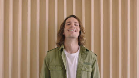 portrait of handsome young caucasian man laughing cheerful confident looking at camera relaxed male with long hair wooden backgroud