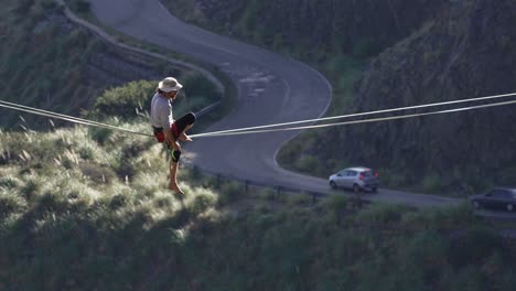 a man balancing on a highline contemplating a road with cars below