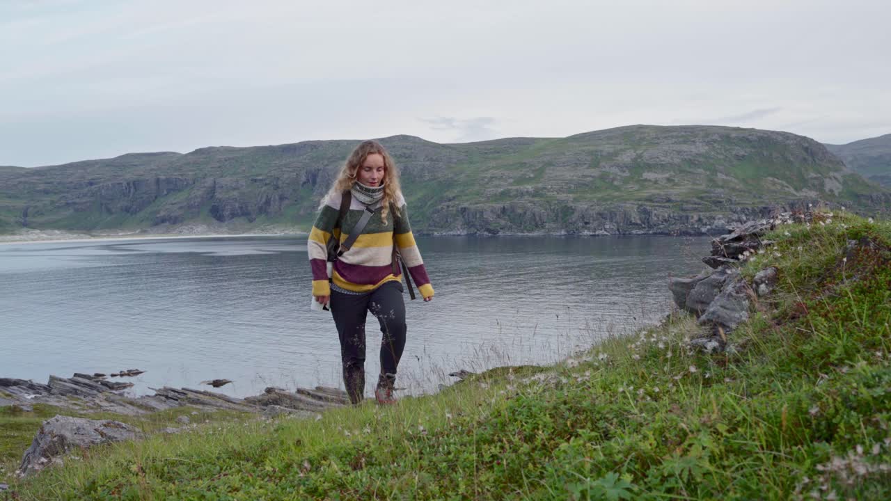 배낭과 카메라를 들고 노르웨이 해안 언덕을 오르는 여성