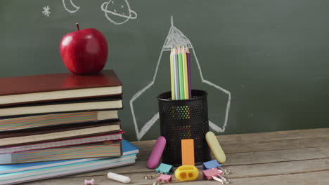 video of school supplies and books on wooden table over blackboard