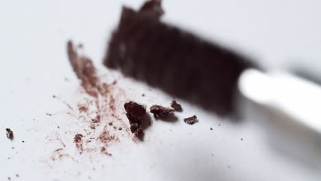 smudging a bit of crumbly dark-brown mascara, using a ball-tipped bristle applicator on an empty whiteboard palette