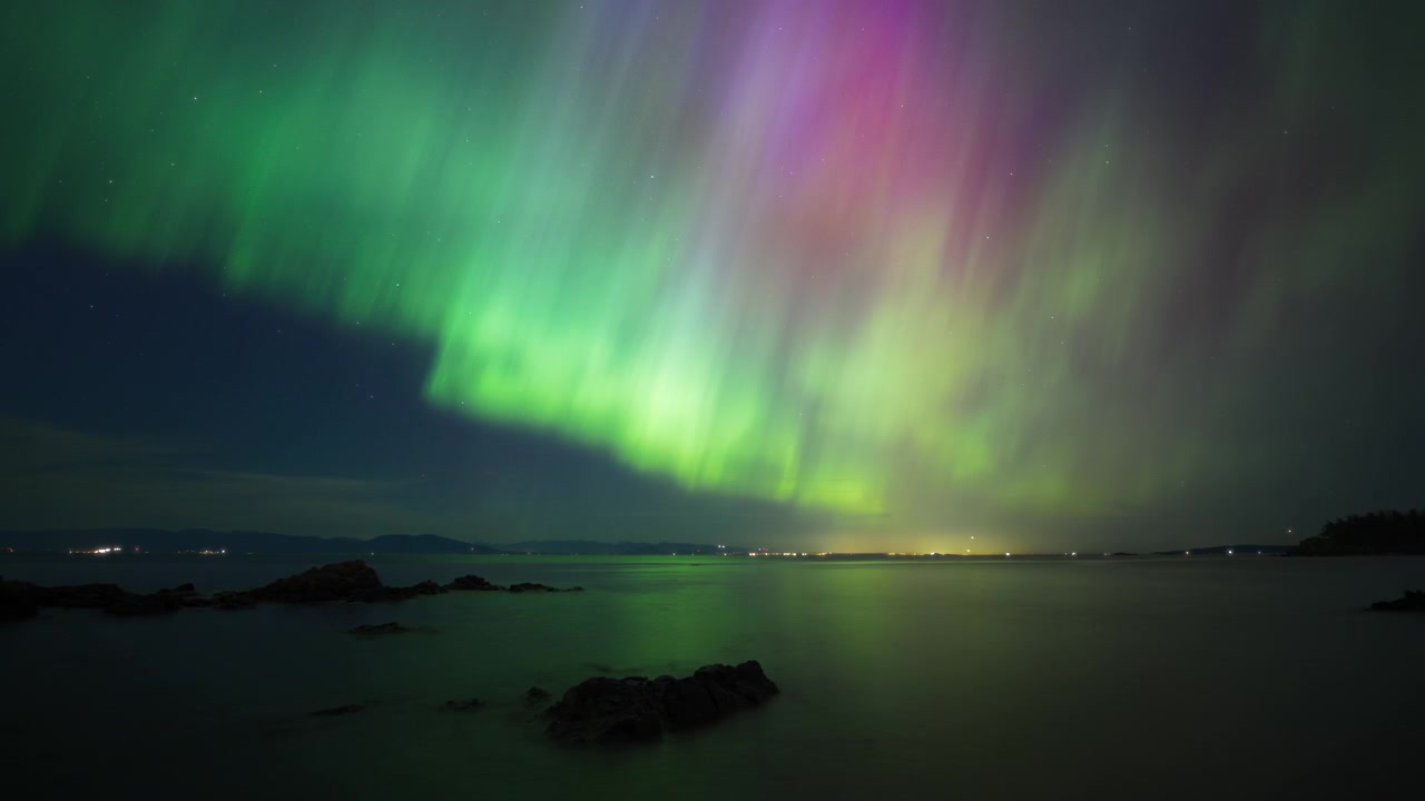 Aurore boreali colorate che danzano sopra l'oceano sull'isola di Vancouver, Canada.