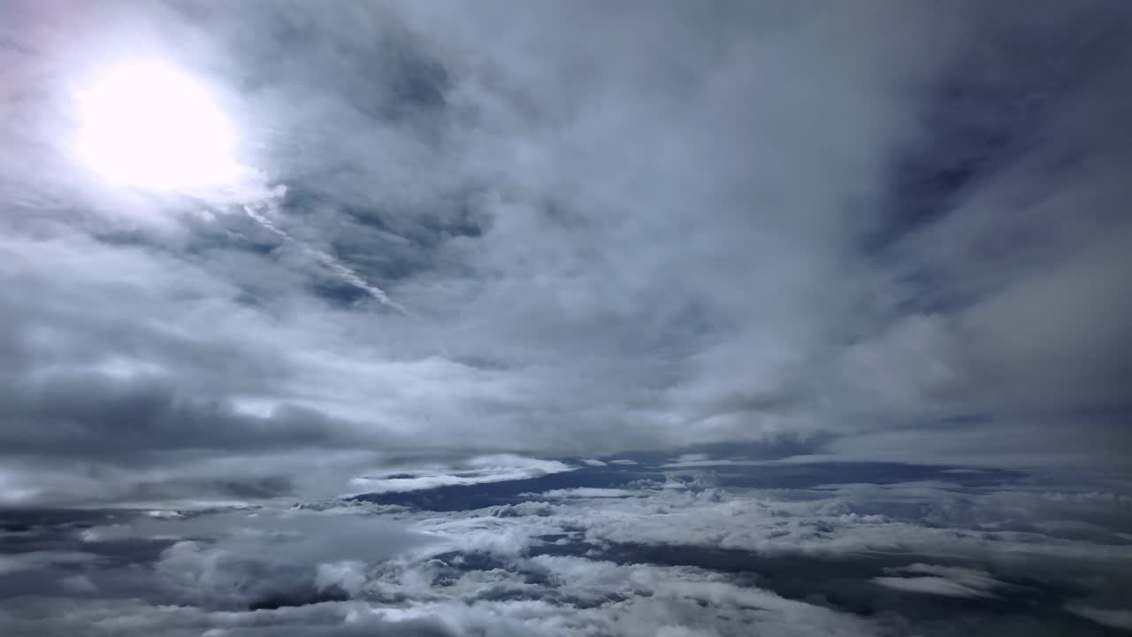 Tampilan pilot imersif yang diambil dari pesawat jet saat terbang dengan kecepatan supersonik melalui lapisan awan stratus yang halus, dengan matahari tertutup yang memudar bersinar di atas langit biru. Bidikan 4K