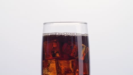 close up of ice cubes falling in a glass of fresh cola on white background