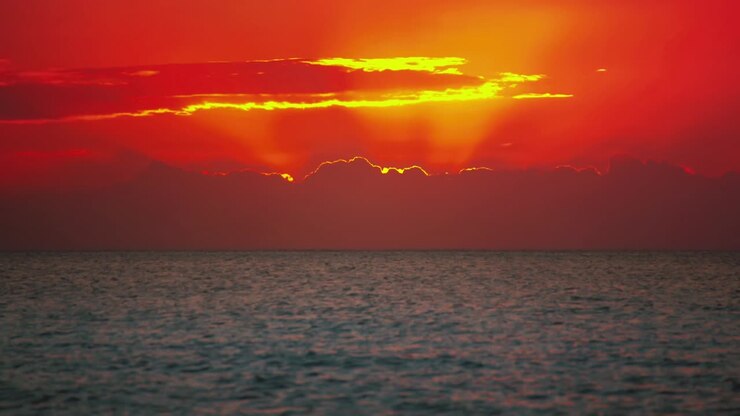 Cinemagraph / nahtlose Videoschleife eines leuchtend roten Sonnenuntergangs an einem abgelegenen natürlichen Sandstrand an der Küste der Toskana in Italien mit dramatischem Himmel und Panoramablick auf das Meer. Blaues und türkisfarbenes Wasser an diesem malerischen Natur-Urlaubsort.