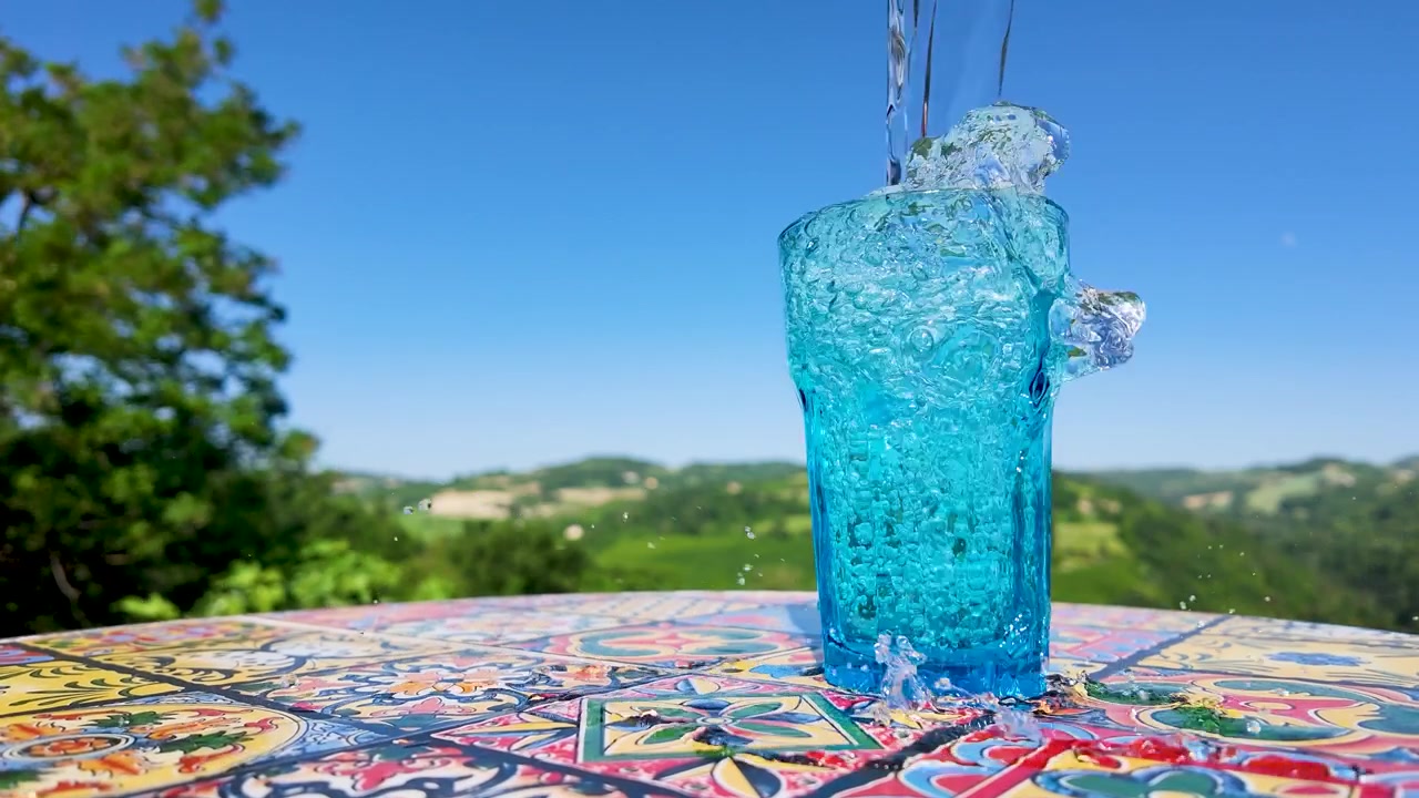 Carbonated water fills a blue glass on a colorful mosaic table under bright sunlight.