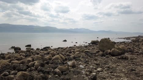 Mysterious-creepy-Martian-mountain-range-rocky-alien-stone-beach-coastline-moving-low-forward-over-ocean