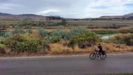 mature man rides bicycle through a park and onto a paved nature trail - aerial view