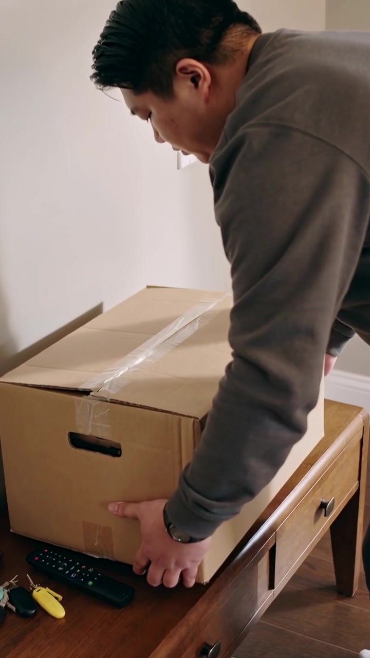 Vertical video: Bringing man in grey shirt lowering taped box onto console to set down, copy space