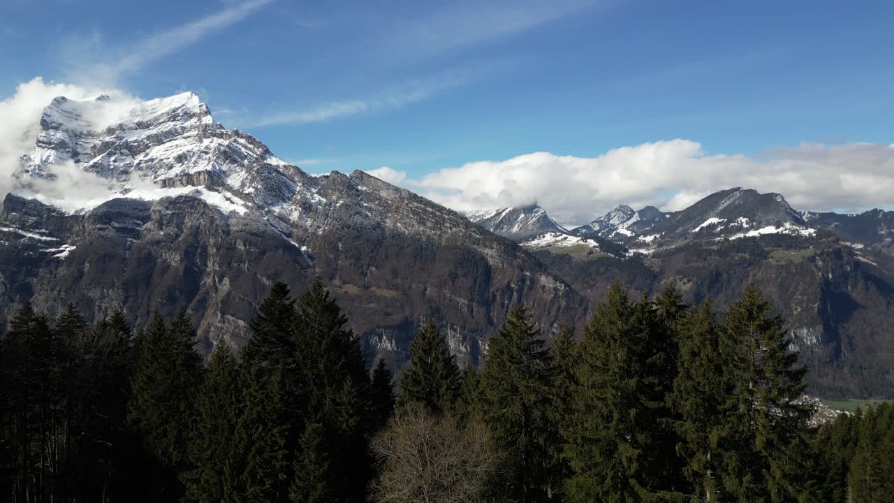 Beautiful aerial drone forward moving shot of snow covered mountain peaks alongside a valley in Fronalpstock Switzerland Glarus on a sunny day