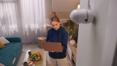woman uses laptop in her living room with a security camera in view