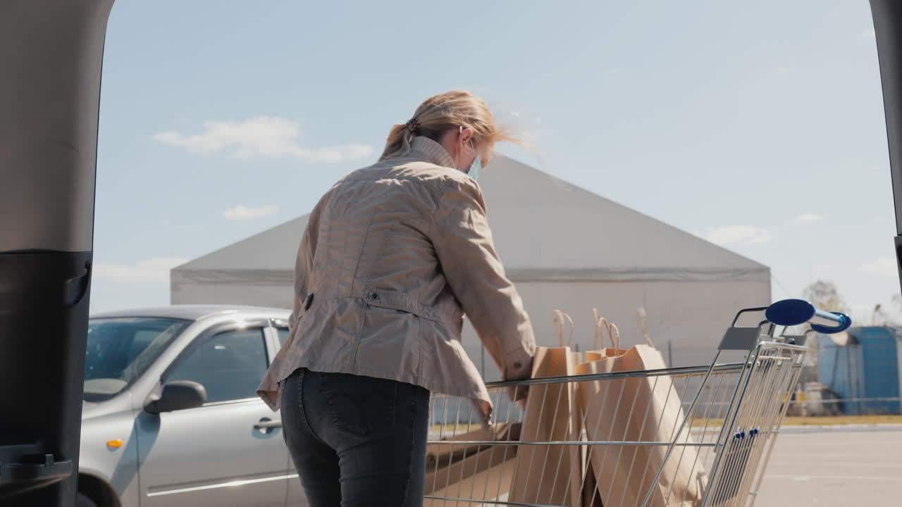전염병 동안 쇼핑 - 여자는 차 트렁크에 음식 가방을 넣습니다 1