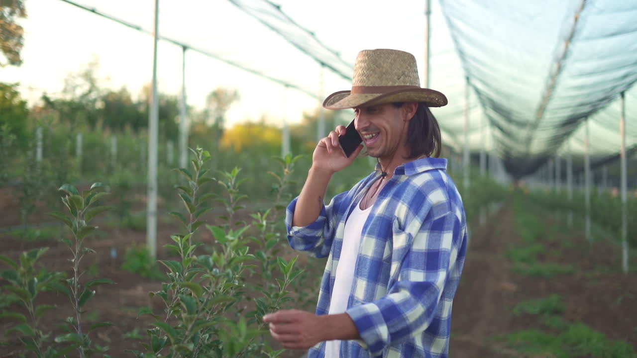 A farmer talks on his phone in an orchard