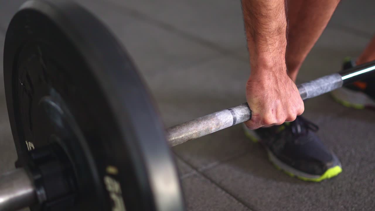 Primo piano di un uomo che stringe e solleva un bilanciere in palestra