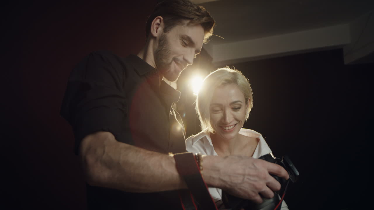 vista de cerca de un fotógrafo que muestra fotos de una sesión de fotos a la joven modelo rubia en la pequeña pantalla de la cámara en el estudio oscuro