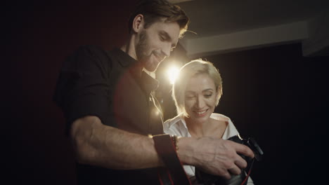 close-up view of a photographer man showing photos of photoshoot to the young blond woman model on the little camera screen in the dark studio