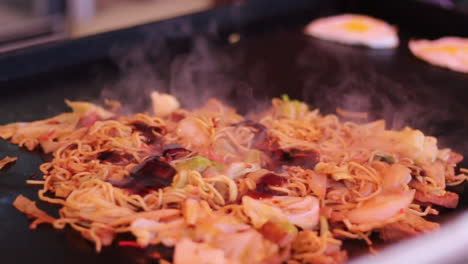 street seller frying japanese street food yakisoba and pouring brown sauce on the teppan