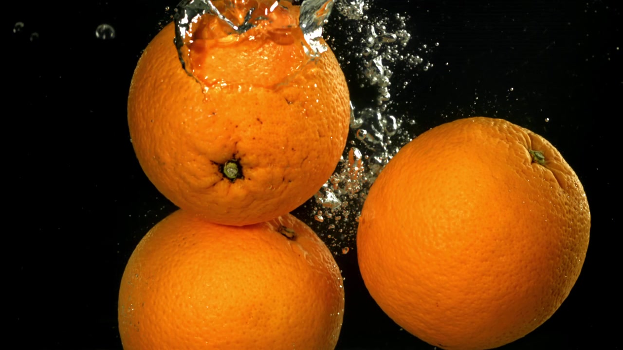 Tre arance fresche che cadono nell'acqua con bolle