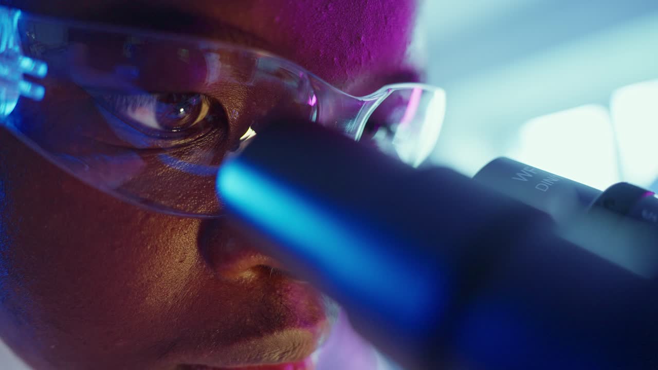 Fokuseret forsker kigger i mikroskop i moderne laboratorium.