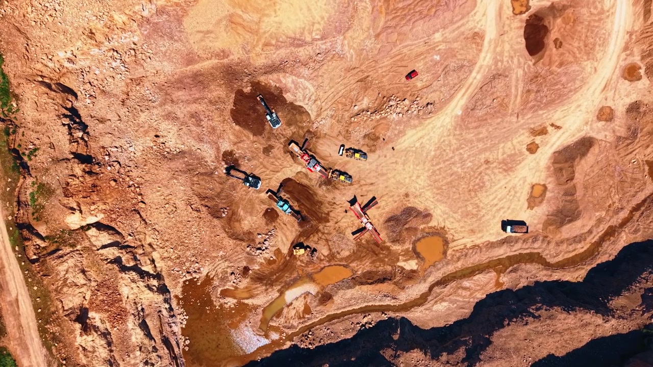 Straight down aerial view of stone quarry pit. Overhead drone perspective of active mining site with excavators trucks and muddy terrain.