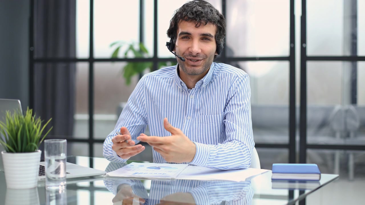 Professionista con cuffie che parla e sorride alla scrivania dell'ufficio