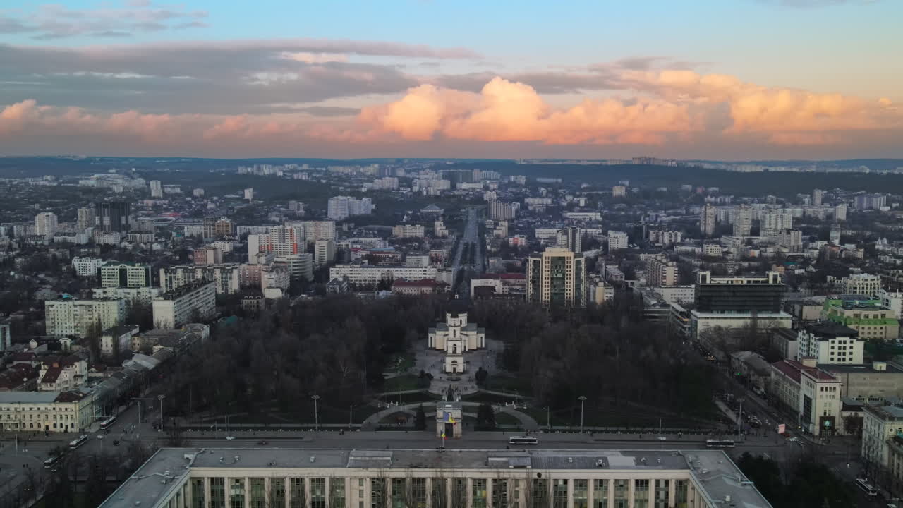 Aerial drone view of Chisinau at sunset. Panorama view of the city center with the Government House and central park, multiple buildings, roads with moving cars, bare trees. Moldova