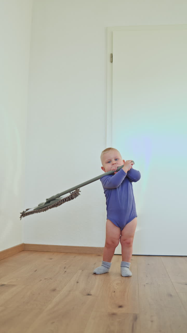 Little boy toddler washes the floor with a mop. Child helps clean the floor. Boy in a cotton bodysuit