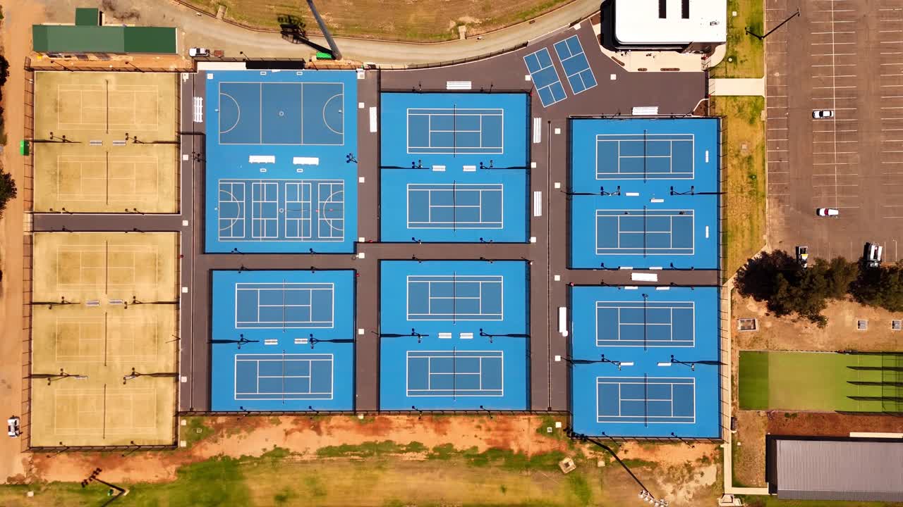 Udendørs sportsbaner danner et markant geometrisk mønster med klare blå overflader, placeret i et organiseret byrekreativt kompleks, set oppefra.