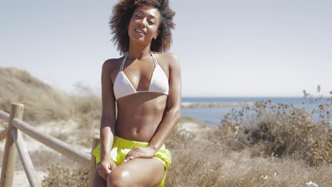attractive sporty woman with curls posing at camera flirty while sitting on fence