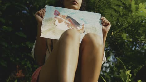 low shot artistic moment: woman presenting colorful sketch in natural setting, sunlit