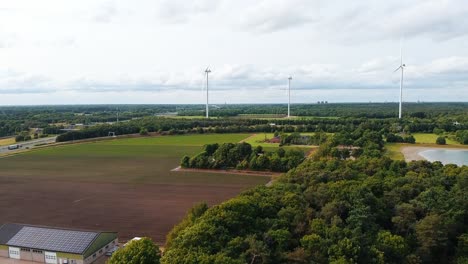 aerial above scenic lake surrounded by trees and farmland with distant highway and windmills in breda, netherlands.