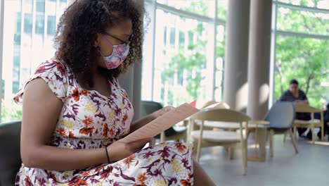 una mujer afroamericana con el cabello corto se relaja en una cafetería con una máscara protectora durante la pandemia de covid-19