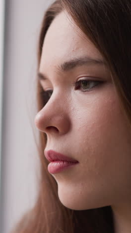 una mujer angustiada mira por la ventana de cerca. una mujer triste se ocupa de los síntomas de trauma psicológico en casa. expresión de estado de ánimo pensativo por modelo