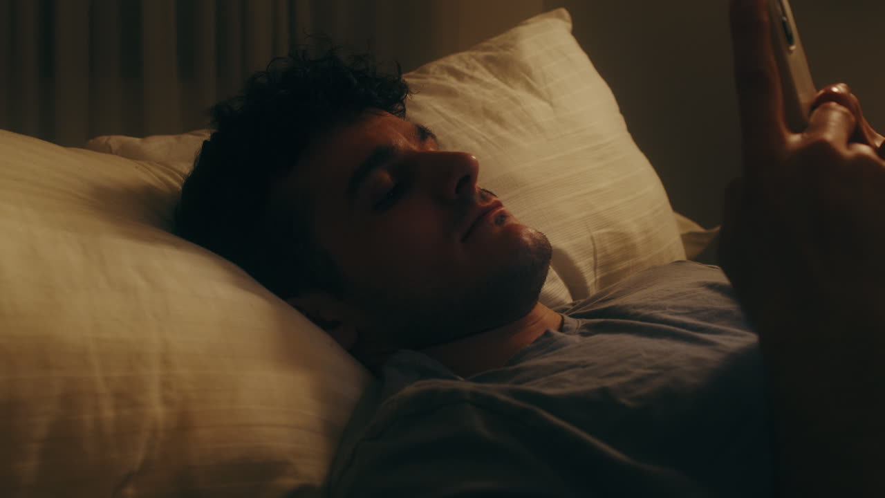 hombre solitario mirando el teléfono mientras se acuesta en la cama