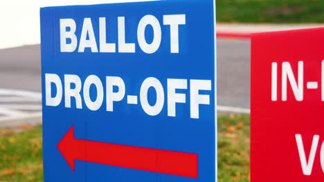 blue ellection ballot drop-off sign with red arrow pointing left and blowing in the wind outside in parking lot