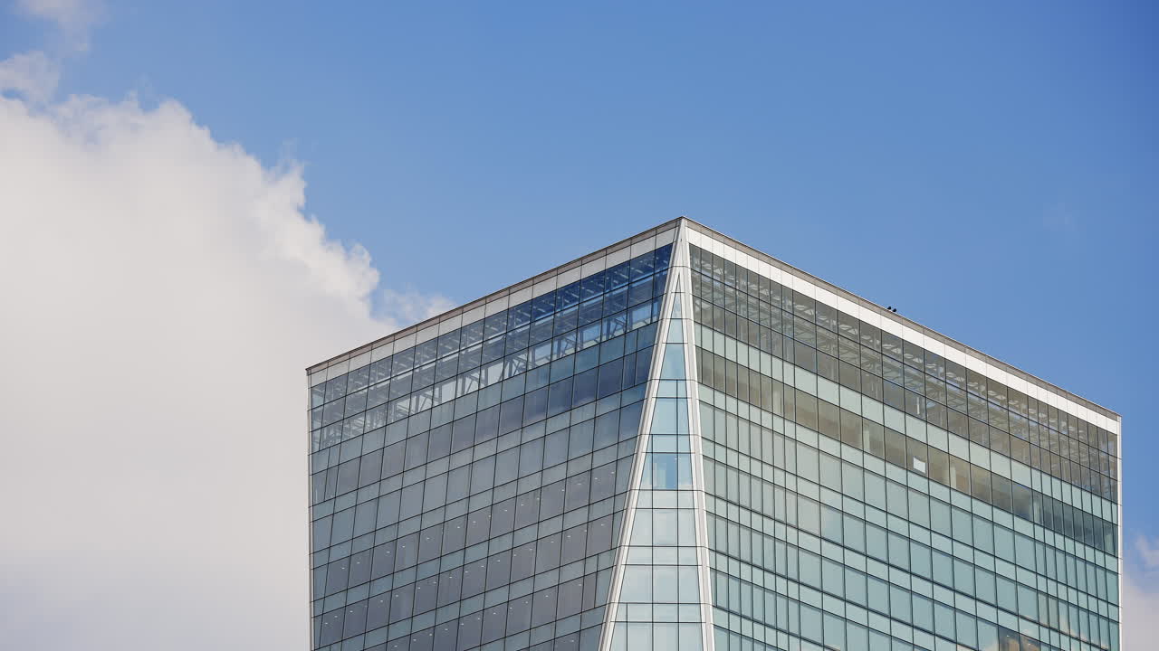 Time lapse of the clouds forming and passing over a huge skyscraper building on the downtown comercial area of big city with blue sky in the background