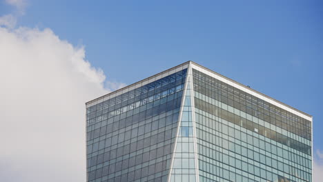 Time-lapse-of-the-clouds-forming-and-passing-over-a-huge-skyscraper-building-on-the-downtown-comercial-area-of-big-city-with-blue-sky-in-the-background