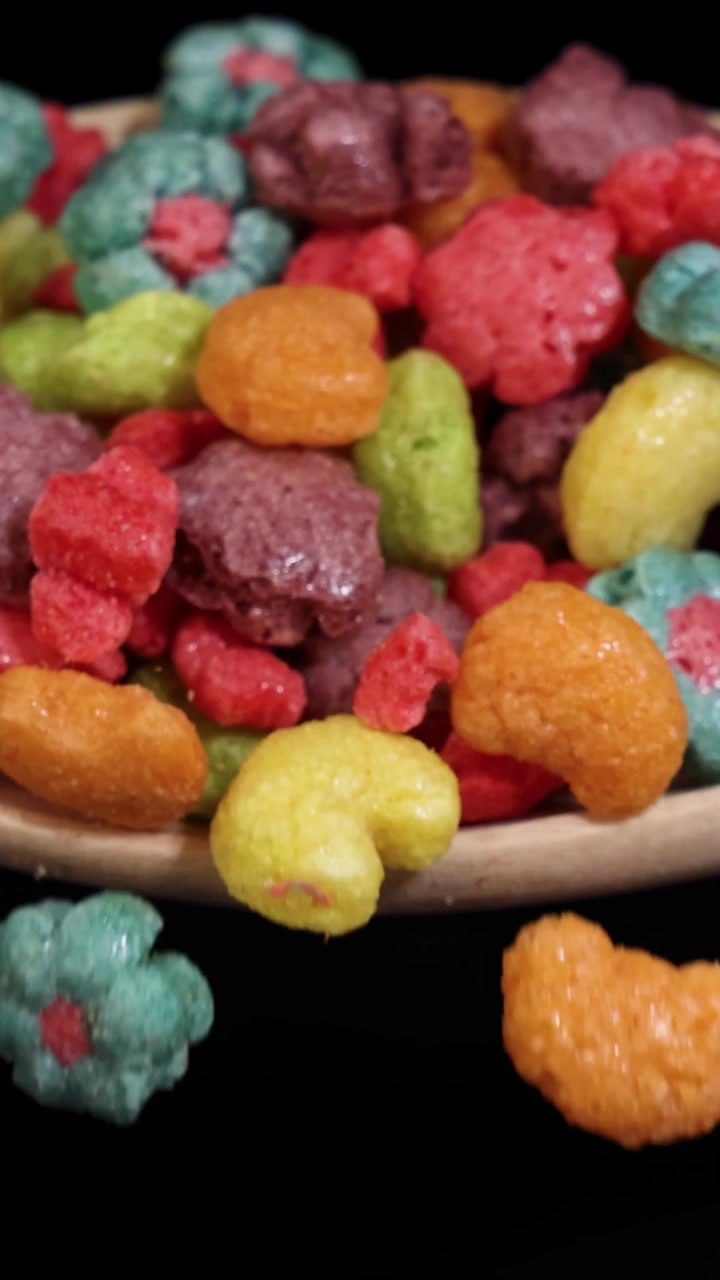 Pedaços de cereal vibrantes caindo de uma colher contra um fundo preto, capturados em câmera lenta com iluminação dramática.