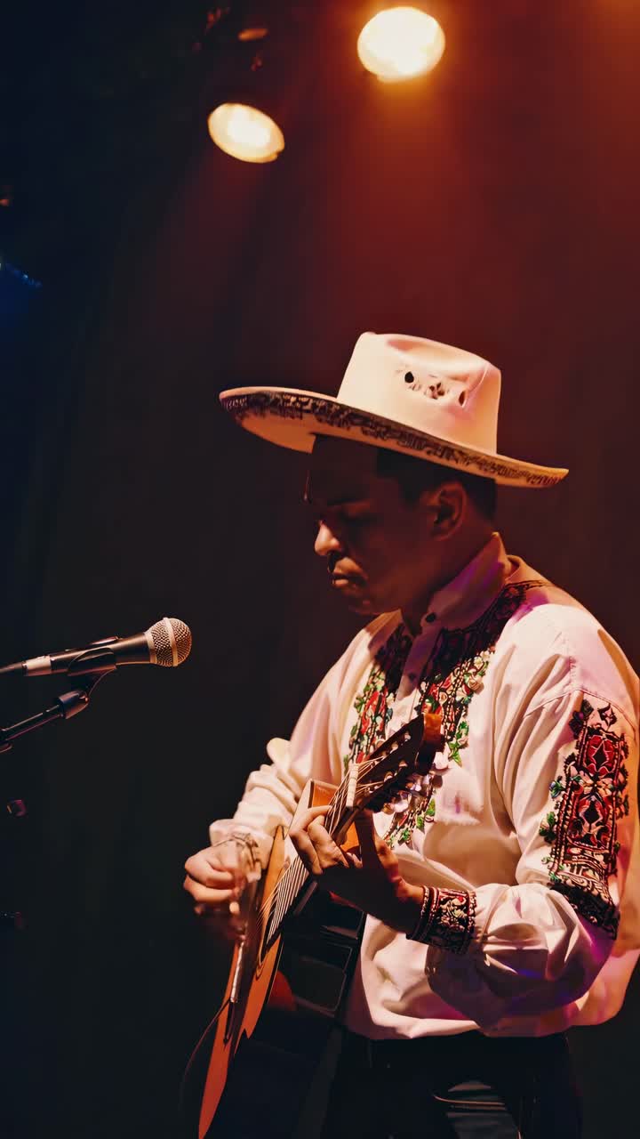 Low-angle shot of a musician in traditional attire playing guitar under warm stage lights