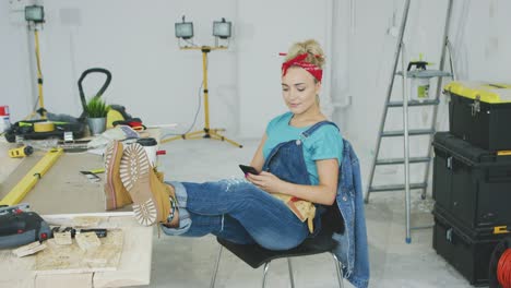 Woman-resting-with-smartphone-at-carpenter-workbench-