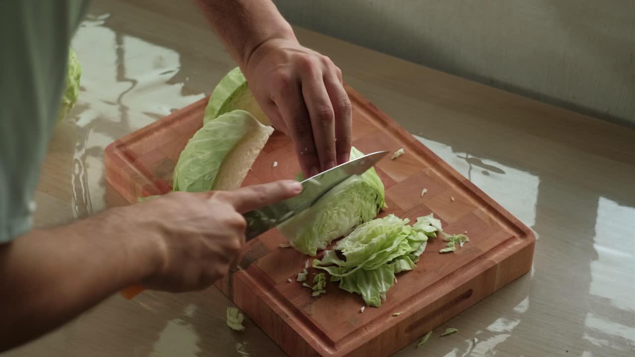 Close-up static shot of hands finely slicing cabbage quarters on wooden chopping board.