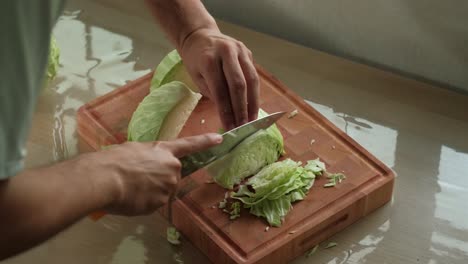 close-up static shot of hands finely slicing cabbage quarters on wooden chopping board.
