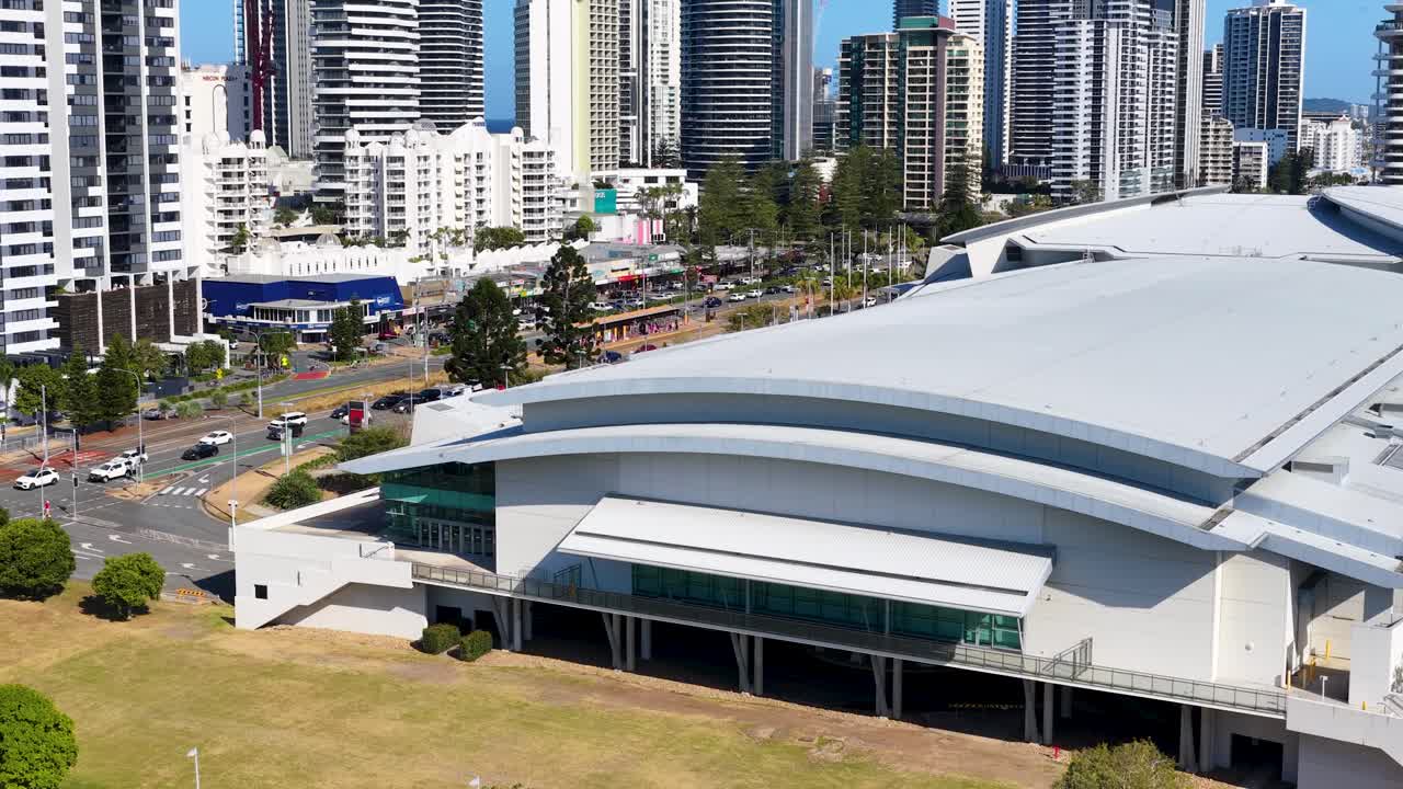 Ripresa aerea diurna con drone che sorvola un centro congressi, i grattacieli della città e le trafficate strade della Gold Coast