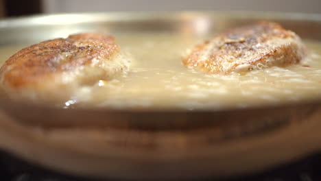 boneless chicken breasts simmering in a pan in a savory sauce - slow dolly forward reveal