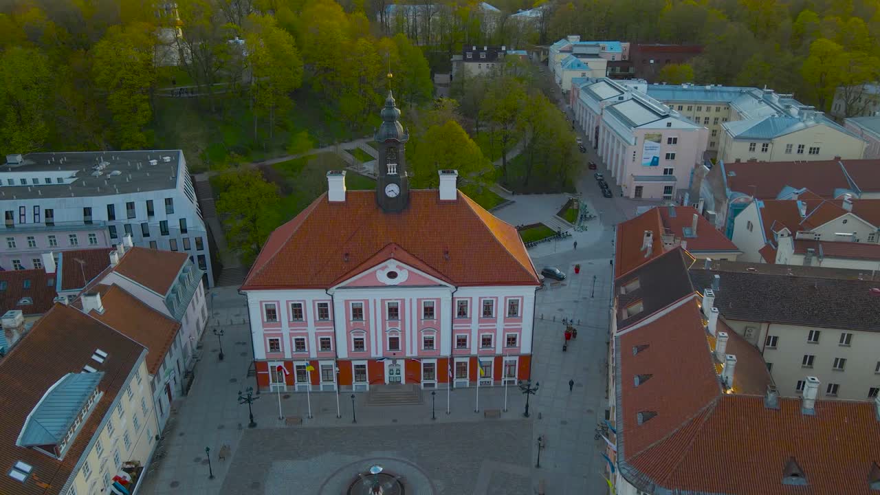Aerial orbit of Town Hall Square centre of Tartu city, meeting place for people. Classical buildings line the square and in middle is fountain. Baroque hall tower with bells and clock, urban greenery