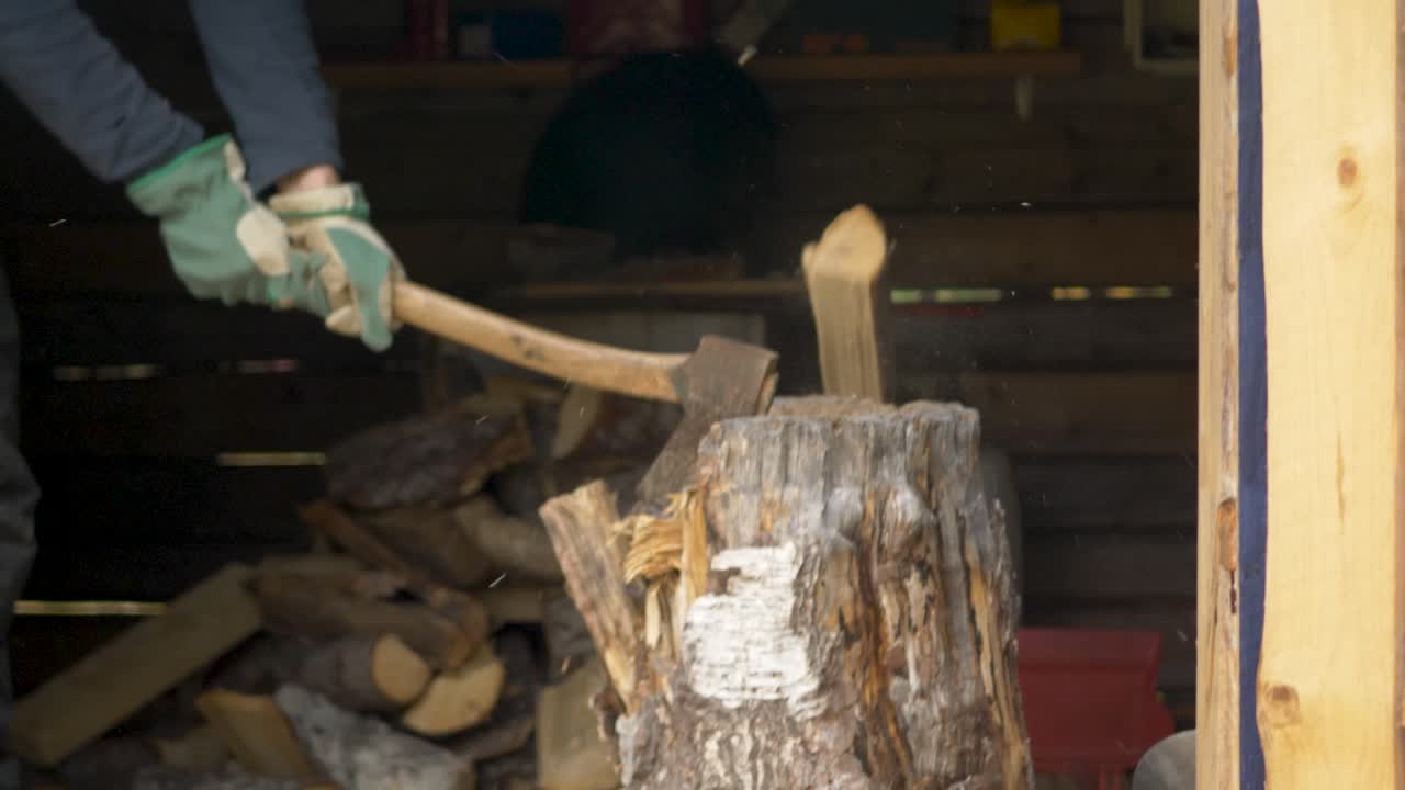 Man Splitting and Cutting Firewood With Hatchet in Woodshed - Medium tilt down slow-motion shot