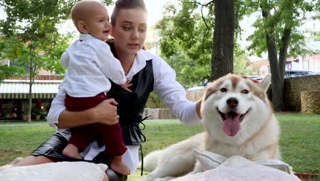 family and pet, little boy in suit on hands of mother stroking the husky on green grass in a park