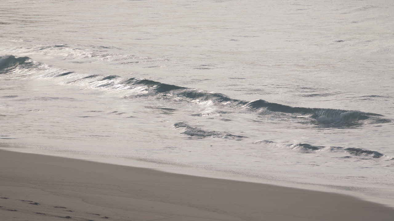 작은 파도가 완벽하게 매끄러운 모래사장을 펼치고 아무도 통찰력이 없습니다.